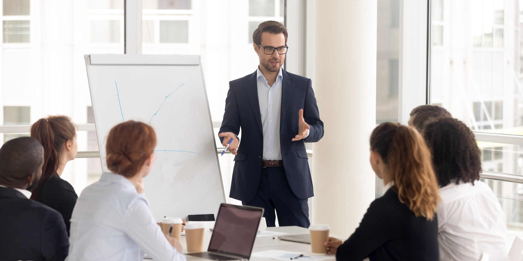 Male business coach speaker in suit give flipchart presentation, speaker presenter consulting training persuading employees client group, mentor leader explain graph strategy at team meeting workshop